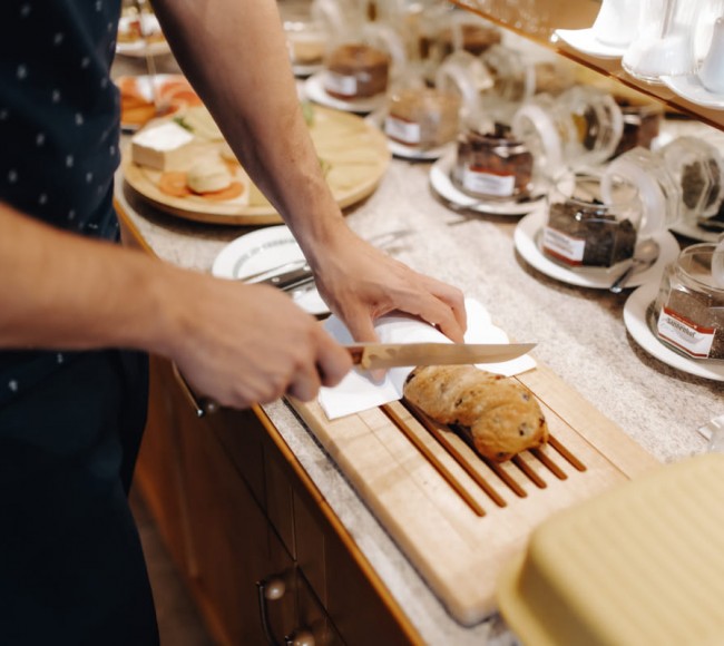 Mann beim Brot aufschneiden beim Frühstücksbuffet